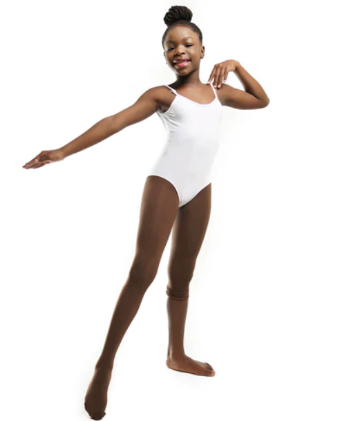 A photo of a happy young Black girl with dark skin posing in a white leotard and Blendz dark brown convertible dance tights in the color “confident cocoa” showing the tights over one foot and up her leg.